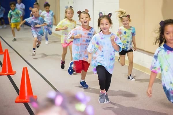 Young children in tie dye shirts running in a line in school gymnasium